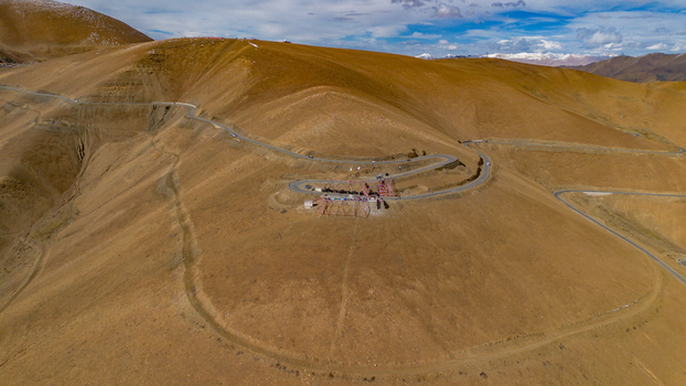 Aerial view of the winding mountain road at Gawula pass surrounded by barren golden hills and distant snow capped peaks in Shigatse Tibet China.