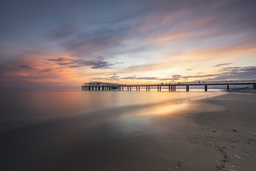View of the modern pier extending into the calm sea under a vibrant sunset sky with orange and purple clouds over the sandy beach in Lido di Camaiore Tuscany Italy.