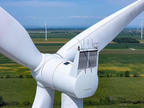Aerial view of a white wind turbine nacelle with sensor equipment against a backdrop of green agricultural fields and blue sky in Lakeshore Ontario Canada. Aerial view of a white wind turbine nacelle with sensor equipment against a backdrop of green agricultural fields and blue sky in Lakeshore Ontario Canada.