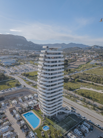 Aerial view of modern high rise building with white curved balconies a swimming pool and an adjacent recreational vehicle park in Calp Valencian Community Spain. Aerial view of modern high rise building with white curved balconies a swimming pool and an adjacent recreational vehicle park in Calp Valencian Community Spain.
