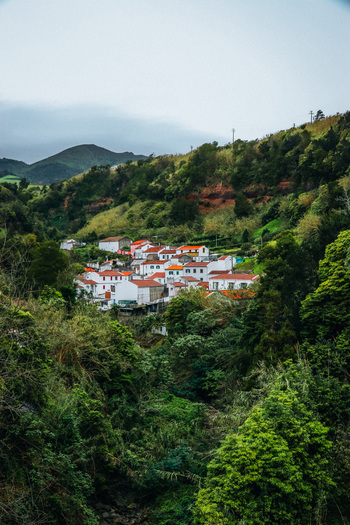 View of a cluster of white houses with red roofs nestled amid vibrant green vegetation under a cloudy sky Furnas Azores Portugal.
