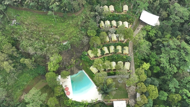 Aerial view of Glamping Menoreh featuring rows of luxury tents nestled in a lush green forest with a turquoise swimming pool in Kecamatan Samigaluh Daerah Istimewa Yogya Indonesia. Aerial view of Glamping Menoreh featuring rows of luxury tents nestled in a lush green forest with a turquoise swimming pool in Kecamatan Samigaluh Daerah Istimewa Yogya Indonesia.