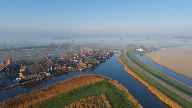 Aerial view of the historic village of Schermerhorn with traditional houses along a canal and windmills shrouded in morning mist Schermerhorn North Holland Netherlands. Aerial view of the historic village of Schermerhorn with traditional houses along a canal and windmills shrouded in morning mist Schermerhorn North Holland Netherlands.