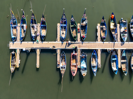Aerial view of fishing boats berthed in a row casting elongated shadows on the dark water in Porta de Abrigo da Torreira Torreira Aveiro Portugal. Aerial view of fishing boats berthed in a row casting elongated shadows on the dark water in Porta de Abrigo da Torreira Torreira Aveiro Portugal.