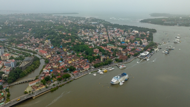 Aerial view of the Mandovi River with a cruise ship docked near the city of Panaji featuring dense urban architecture and the Atal Setu Goa bridge Panaji Goa India.