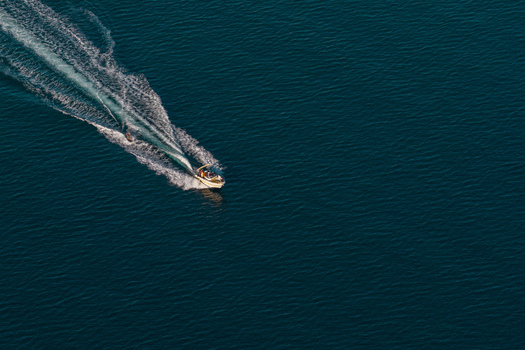 Aerial view of a motorboat creating a white wake while towing a water skier on the deep blue Mediterranean Sea near Antibes Provence Alpes Cote d Azur France. Aerial view of a motorboat creating a white wake while towing a water skier on the deep blue Mediterranean Sea near Antibes Provence Alpes Cote d Azur France.