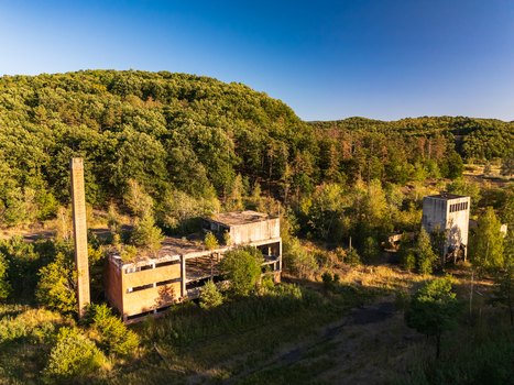 Aerial view of abandoned coal loading facility ruins surrounded by summer forest in Rakoczibanya Hungary with a concrete chimney and weathered industrial buildings. Aerial view of abandoned coal loading facility ruins surrounded by summer forest in Rakoczibanya Hungary with a concrete chimney and weathered industrial buildings.