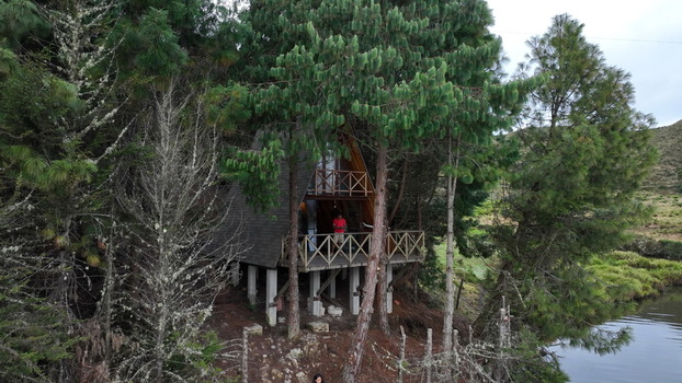 Aerial view of an A frame cabin nestled among pine trees near the Corani lake with a person standing on the wooden balcony in Cochabamba Departamento de Cocha Bolivia.