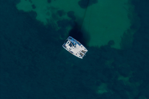 Aerial view of a white catamaran sailing on clear turquoise and deep blue waters off the coast of Antibes Provence Alpes Cote d Azur France. Aerial view of a white catamaran sailing on clear turquoise and deep blue waters off the coast of Antibes Provence Alpes Cote d Azur France.