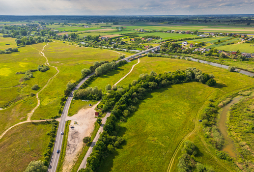 Aerial view of Nadwarcianski Park Krajobrazowy featuring a winding road a bridge over the Warta River lush green meadows and scattered trees in Lad Greater Poland Voivod Poland. Aerial view of Nadwarcianski Park Krajobrazowy featuring a winding road a bridge over the Warta River lush green meadows and scattered trees in Lad Greater Poland Voivod Poland.