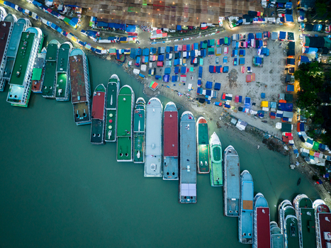 Aerial view of boats docked along the riverbank contrasting with the vibrant market tents creating a lively scene Charmonai Barisal Division Bangladesh. Aerial view of boats docked along the riverbank contrasting with the vibrant market tents creating a lively scene Charmonai Barisal Division Bangladesh.