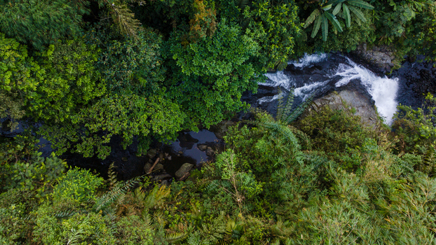 Aerial view of Gomblang Waterfall flowing through dense tropical jungle with lush green foliage and rushing white water in Kecamatan Kedungbanteng Jawa Tengah Indonesia. Aerial view of Gomblang Waterfall flowing through dense tropical jungle with lush green foliage and rushing white water in Kecamatan Kedungbanteng Jawa Tengah Indonesia.