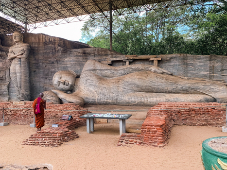Sri Lanka 21 April 2024 View of the ancient Gal Vihara rock cut reclining Buddha statue and standing Buddha with a monk in orange robes standing before the historic stone carvings.