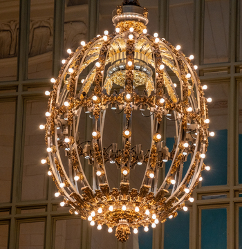 View of the ornate spherical chandelier with glowing light bulbs and intricate gold metalwork inside Grand Central Terminal New York New York United States. View of the ornate spherical chandelier with glowing light bulbs and intricate gold metalwork inside Grand Central Terminal New York New York United States.