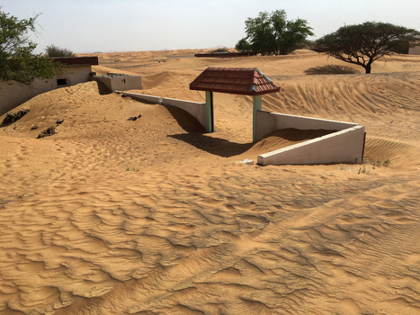 View of abandoned buildings and a small gate with a red roof partially buried by shifting desert sand dunes in Dubai Dubai United Arab Emirates. View of abandoned buildings and a small gate with a red roof partially buried by shifting desert sand dunes in Dubai Dubai United Arab Emirates.