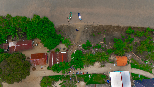 Aerial view of a coastal village with small houses palm trees and boats moored on the sandy riverbank in Minima Rivers Nigeria.