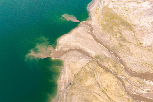 Aerial view of brown mineral sediment flowing into turquoise water of a post industrial lake with barren sandy shores in Poland.