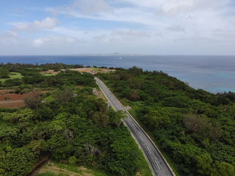 Aerial view of a new asphalt road winding through the lush green landscape of Sesoko Island with the blue sea and the Motobu Peninsula visible in the distance Motobu Okinawa Japan. Aerial view of a new asphalt road winding through the lush green landscape of Sesoko Island with the blue sea and the Motobu Peninsula visible in the distance Motobu Okinawa Japan.
