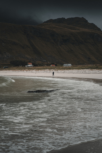 View of Haukland Beach with a person walking along the sandy shore under a moody sky with mountains in the background in Leknes Nordland Norway. View of Haukland Beach with a person walking along the sandy shore under a moody sky with mountains in the background in Leknes Nordland Norway.