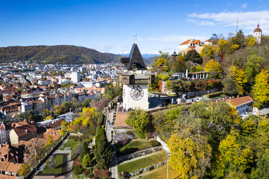 Aerial view of the iconic clock tower the Grazer Uhrturm standing tall against a backdrop of autumnal hues and the cityscape below Graz Styria Austria.