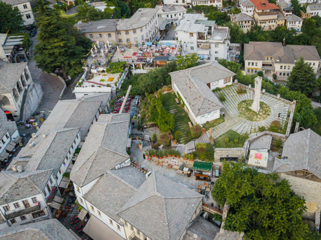 Aerial view of the historic old town featuring a stone monument traditional stone roofed houses and people at outdoor cafes in Gjirokaster Gjirokaster County Albania. Aerial view of the historic old town featuring a stone monument traditional stone roofed houses and people at outdoor cafes in Gjirokaster Gjirokaster County Albania.