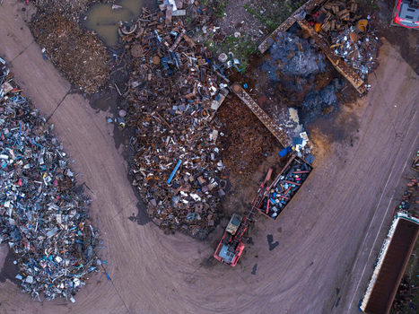 Aerial view of a large industrial scrap yard featuring massive piles of sorted metal rusted machinery and dirt access paths in Charleroi Wallonia Belgium.