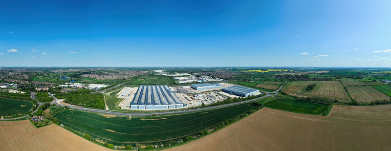 Aerial view of Symmetry Park logistics hub featuring large modern warehouses surrounded by green agricultural fields under a clear blue sky Kettering England United Kingdom. Aerial view of Symmetry Park logistics hub featuring large modern warehouses surrounded by green agricultural fields under a clear blue sky Kettering England United Kingdom.