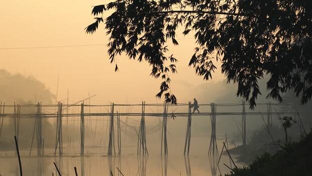 View of a person walking on a bamboo bridge at sunrise Bangladesh.