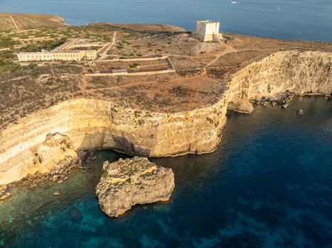 Aerial view of the Santa Maria Tower stands sentinel atop rugged cliffs overlooking the azure waters of the Blue Lagoon Comino Malta. Aerial view of the Santa Maria Tower stands sentinel atop rugged cliffs overlooking the azure waters of the Blue Lagoon Comino Malta.