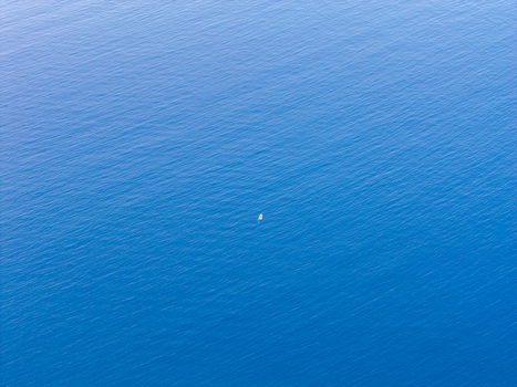 Aerial view of a small boat floating in the vast blue waters of the Tyrrhenian Sea near the Riserva Naturale Orientata dello Zingaro San Vito Lo Capo Sicilia Italy. Aerial view of a small boat floating in the vast blue waters of the Tyrrhenian Sea near the Riserva Naturale Orientata dello Zingaro San Vito Lo Capo Sicilia Italy.