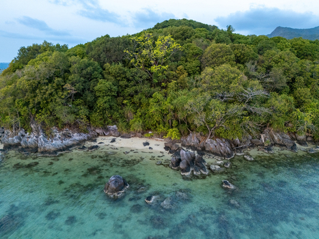 Aerial view of a lush tropical island coastline with dense green forest rocky outcrops and clear turquoise water in Karimunjawa Central Java Indonesia. Aerial view of a lush tropical island coastline with dense green forest rocky outcrops and clear turquoise water in Karimunjawa Central Java Indonesia.
