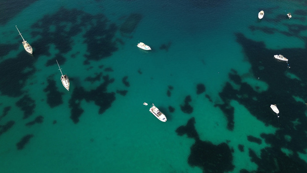 Aerial view of several sailboats and motorboats anchored in the clear turquoise waters of the Mediterranean Sea off the coast of Malta. Aerial view of several sailboats and motorboats anchored in the clear turquoise waters of the Mediterranean Sea off the coast of Malta.
