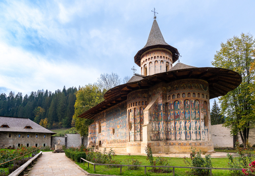 View of Voronet Monastery with its iconic exterior frescoes stone walls and surrounding trees in Voronet Judetul Suceava Romania. View of Voronet Monastery with its iconic exterior frescoes stone walls and surrounding trees in Voronet Judetul Suceava Romania.