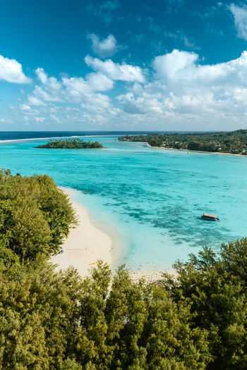 Aerial view of the turquoise lagoon and white sand beach of Rarotonga with lush tropical trees and a small boat Cook Islands. Aerial view of the turquoise lagoon and white sand beach of Rarotonga with lush tropical trees and a small boat Cook Islands.