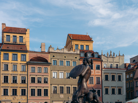 View of the Warsaw Mermaid statue in the Old Town Market Place set against a backdrop of colorful historic townhouses under a clear blue sky in Warsaw Masovian Voivodeship Poland. View of the Warsaw Mermaid statue in the Old Town Market Place set against a backdrop of colorful historic townhouses under a clear blue sky in Warsaw Masovian Voivodeship Poland.