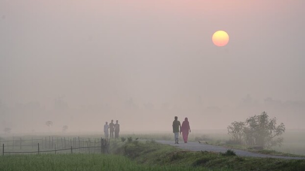 View of people walking through misty fields at dawn Bangladesh.
