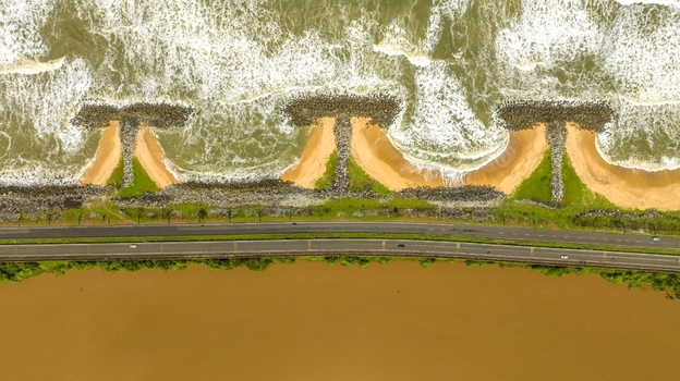 Aerial view of Maravanthe beach featuring a road separating the Arabian Sea and the Souparnika River with T shaped groynes and sandy coastline in Maravanthe Karnataka India. Aerial view of Maravanthe beach featuring a road separating the Arabian Sea and the Souparnika River with T shaped groynes and sandy coastline in Maravanthe Karnataka India.