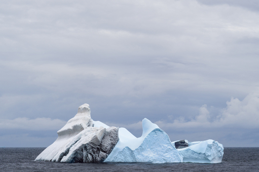 View of a large iceberg floating in the dark ocean under a cloudy sky in the South Orkney Islands. View of a large iceberg floating in the dark ocean under a cloudy sky in the South Orkney Islands.