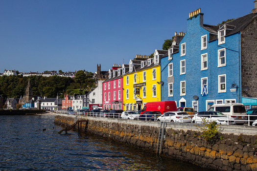 View of the iconic colorful houses along the harbor front with parked cars and a stone sea wall Tobermory Scotland United Kingdom.