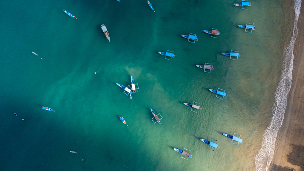 Aerial view of Prigi Beach with numerous traditional fishing boats floating in clear turquoise water along the sandy coastline in Kecamatan Watulimo Jawa Timur Indonesia. Aerial view of Prigi Beach with numerous traditional fishing boats floating in clear turquoise water along the sandy coastline in Kecamatan Watulimo Jawa Timur Indonesia.