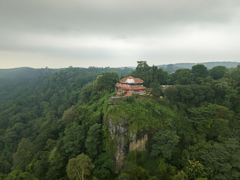 Aerial view of a vibrant red roofed building perched atop a dramatic cliff surrounded by dense lush green forest under a cloudy sky Curugsewu Central Java Indonesia. Aerial view of a vibrant red roofed building perched atop a dramatic cliff surrounded by dense lush green forest under a cloudy sky Curugsewu Central Java Indonesia.