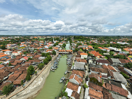 Aerial view of boats docked in a canal cutting through the heart of the city under a vast cloudy sky Jepara Central Java Indonesia.