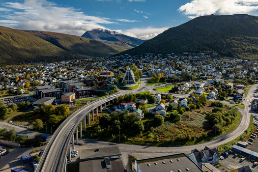 Aerial view of the Arctic Cathedral surrounded by residential buildings a bridge and autumn colored hills in Tromso Troms Norway. Aerial view of the Arctic Cathedral surrounded by residential buildings a bridge and autumn colored hills in Tromso Troms Norway.