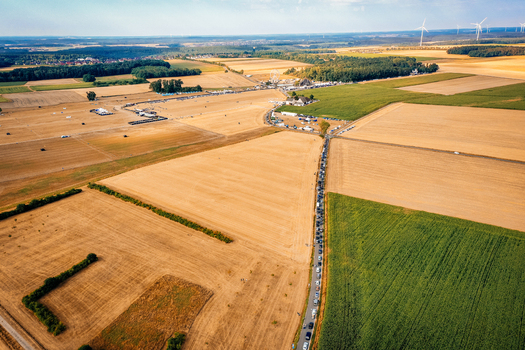 Herzogenaurach Germany 22 July 2022 Aerial view of the Open Beatz Festival site with a long queue of cars on a rural road surrounded by golden fields and wind turbines. Herzogenaurach Germany 22 July 2022 Aerial view of the Open Beatz Festival site with a long queue of cars on a rural road surrounded by golden fields and wind turbines.