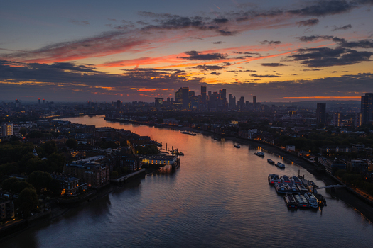 Aerial view of the City of London skyline at sunset with the River Thames reflecting the golden light and skyscrapers silhouetted against a dramatic sky in London England United Kingdom.