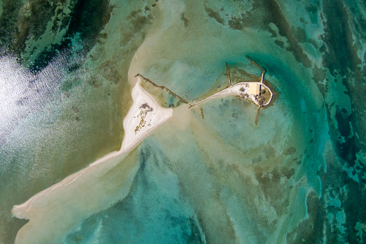Aerial view of the small islet of Agios Nikolaos with its historic chapel surrounded by turquoise waters and sandy shoals in Lefkada Greece.