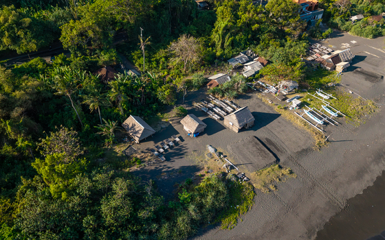 Aerial view of the natural salt maker in Kusamba with traditional thatched roof huts wooden evaporation trays and small outrigger boats on the black sand beach in Kecamatan Dawan Bali Indonesia. Aerial view of the natural salt maker in Kusamba with traditional thatched roof huts wooden evaporation trays and small outrigger boats on the black sand beach in Kecamatan Dawan Bali Indonesia.