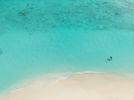 Aerial view of turquoise waters embrace the pristine white sands where two figures stand ankle deep in the shallows Hoarafushi Thiladhunmathee Uthuruburi Maldives. Aerial view of turquoise waters embrace the pristine white sands where two figures stand ankle deep in the shallows Hoarafushi Thiladhunmathee Uthuruburi Maldives.