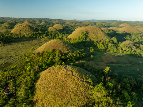 Aerial view of Chocolate Hills with grassy conical mounds lush tropical vegetation and agricultural fields in Batuan Central Visayas Philippines. Aerial view of Chocolate Hills with grassy conical mounds lush tropical vegetation and agricultural fields in Batuan Central Visayas Philippines.