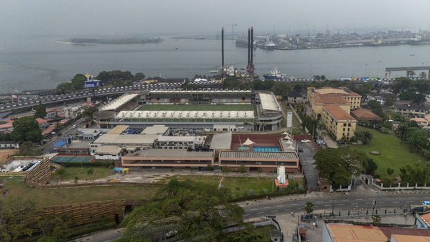 Aerial view of the Onikan Stadium and surrounding urban landscape in Lagos Island featuring a swimming pool sports facilities and the nearby harbor under a hazy sky in Lagos Lagos Nigeria. Aerial view of the Onikan Stadium and surrounding urban landscape in Lagos Island featuring a swimming pool sports facilities and the nearby harbor under a hazy sky in Lagos Lagos Nigeria.